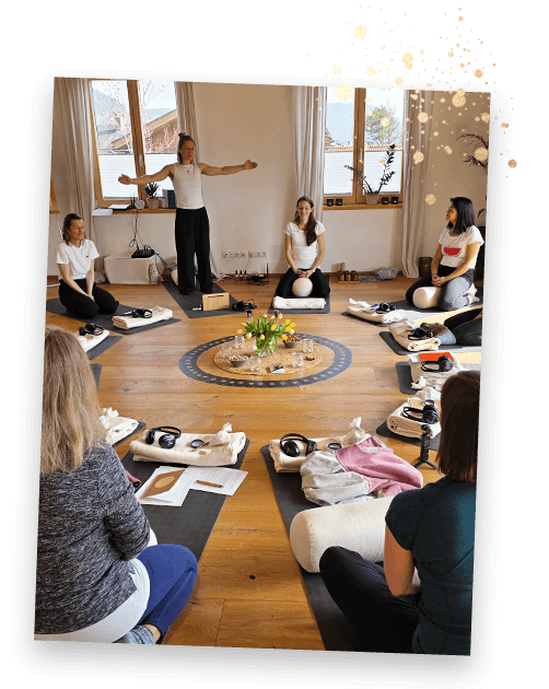 Gruppe sitzt im Kreis auf Yogamatten, Johanna leitet eine Übung im Seminarraum.